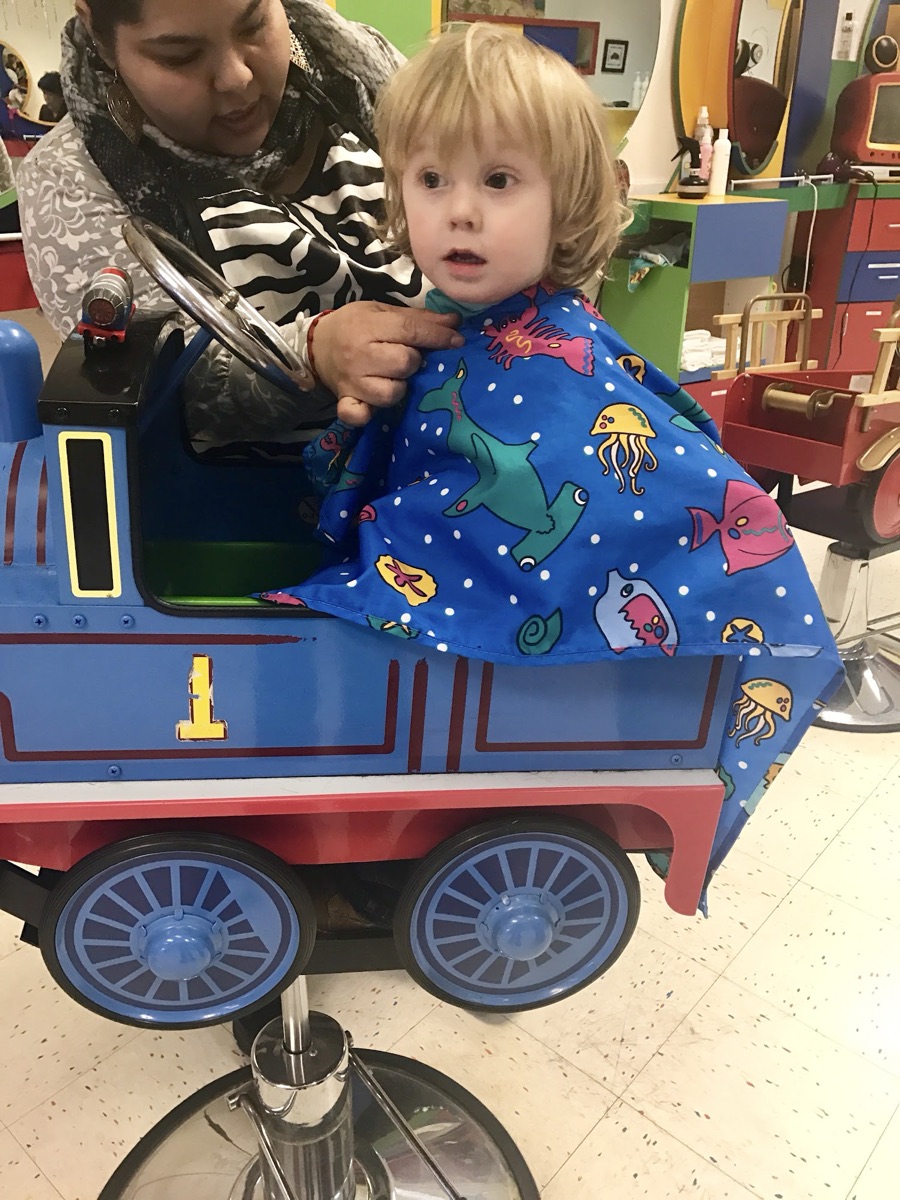 A toddler getting a haircut in the Thomas the Tank Engine chair