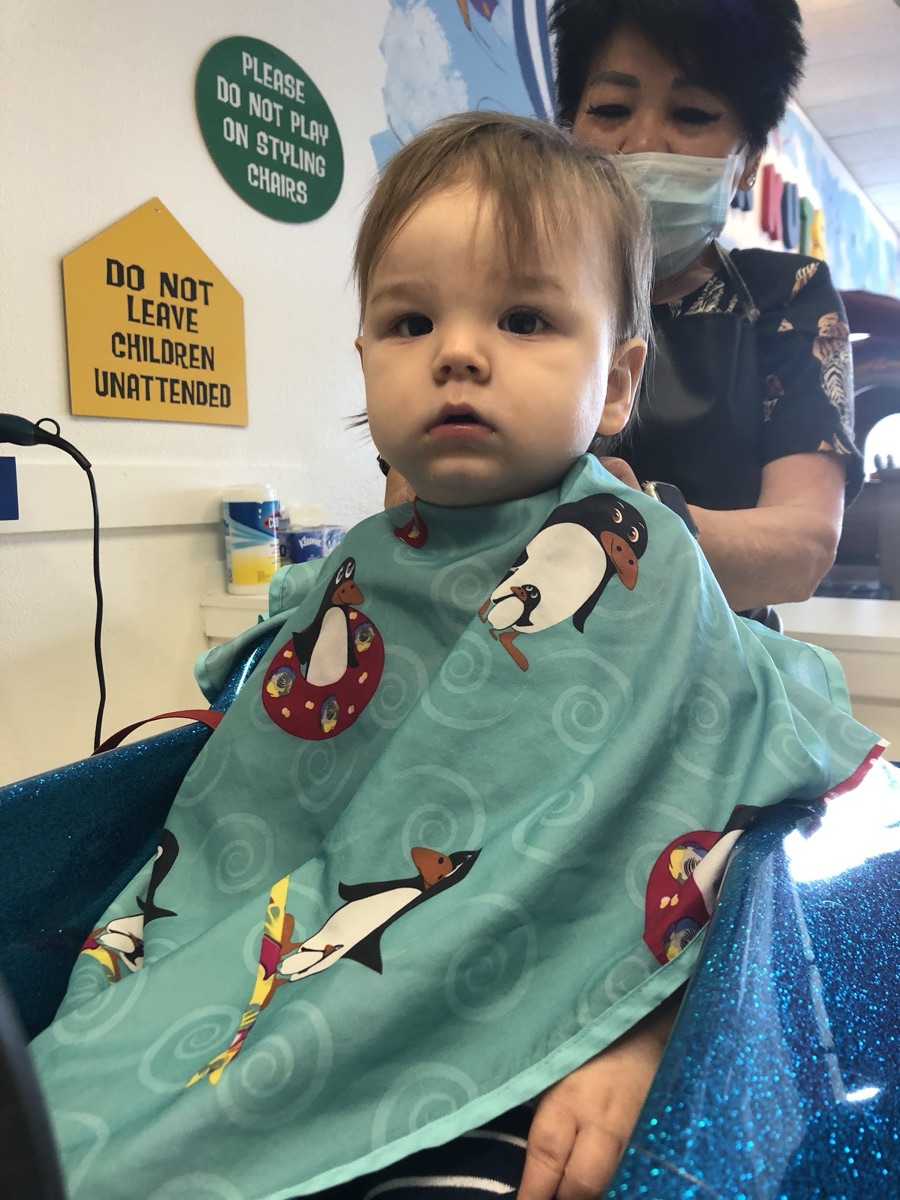 A baby in a penguin cape at their first haircut