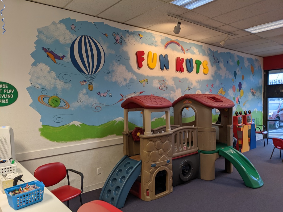 The play area, with a playhouse and slide under the Fun Kuts mural